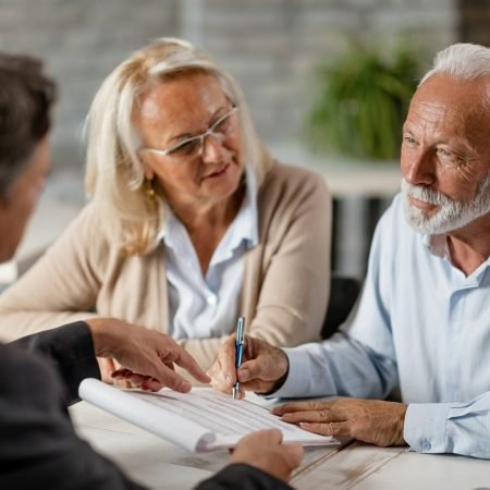 Senior couple signing a contract while having a meeting with ins Mature couple having a meeting with bank manager and signing lease agreement in the office. Focus is mature man.