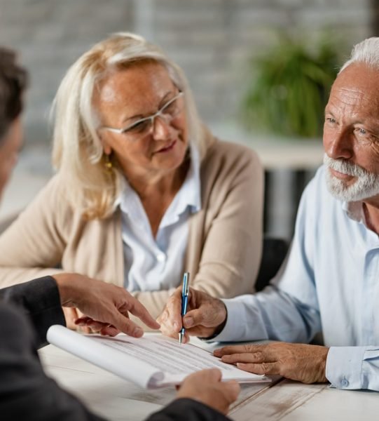 Senior couple signing a contract while having a meeting with ins Mature couple having a meeting with bank manager and signing lease agreement in the office. Focus is mature man.